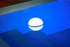A white spherical light with a blue glow sits on a blue surface. Produktbild-Vorschau