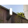 An outdoor wall lamp is mounted on a wooden fence, with greenery and a blue sky in the background. Produktbild-Vorschau
