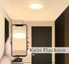 A hand holding a smartphone displaying a ceiling light, with the actual ceiling light visible above. The scene is an indoor hallway with doors. Produktbild-Vorschau