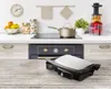 A kitchen counter with a grill in the foreground and kitchen appliances and decor in the background. Produktbild-Vorschau