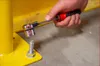 A hand is using a socket wrench to tighten a bolt on a yellow metal structure. Náhled obrázku produktu