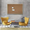 A cork board is mounted on a textured gray wall above two yellow chairs and a wooden bench with books. Produktbild-Vorschau