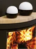 Two white spheres in black bowls sit on a tan surface above a fireplace with flames. Produktbild-Vorschau