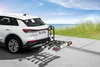 A white car with a bike rack attached to the rear, parked on a paved surface near a beach. Produktbild-Vorschau