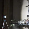 A person is using a smartphone to inspect a large pipe, with a work light on a tripod illuminating the scene. Voir les images du produit