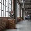 A rustic wooden column with a metal gear sculpture on top, placed in a loft-style living room with large windows and exposed brick. Voir les images du produit