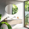 A modern bathroom with a double vanity, a large oval mirror, and lush green plants visible through a large window. Podgląd zdjęcia produktu