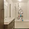 A bathroom scene with a sink, bathtub, and shower area. The product is a black metal shower caddy hanging in the shower. Anteprima dell’immagine prodotto