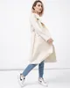 A woman poses in a cream-colored coat and blue jeans against a white background. Produktbild-Vorschau