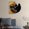 A wall clock with a mountain and forest scene is displayed on a wall above a sofa. Voir les images du produit