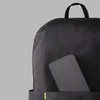 A close-up view of a dark gray backpack with a smartphone partially inserted into an outer pocket. Náhled obrázku produktu