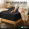 A person sitting on a bed with a black fitted sheet. Produktbild-Vorschau