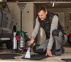 A man is cleaning car mats with a wet vacuum cleaner in a garage. Produktbild-Vorschau