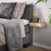 A bedside table with a lamp and a glass of water next to a bed with pillows and a blanket. Produktbild-Vorschau