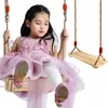A young girl is sitting on a wooden swing, wearing a pink dress and white tights. Náhled obrázku produktu