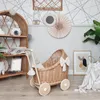 A nursery or play area with a wicker doll stroller, a wicker shelf unit, and wall decorations. Produktbild-Vorschau