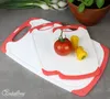 Three cutting boards are stacked on a gray surface, with a tomato and two small yellow peppers on the top board. In the background, there are green onions and a potted plant. Anteprima dell’immagine prodotto