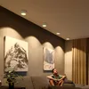 A boy sits on a couch in a living room, looking up at ceiling lights. Two framed mountain pictures hang on the wall. Produktbild-Vorschau