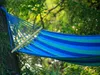 A striped hammock hanging between trees in a lush green outdoor setting. Produktbild-Vorschau