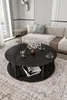 A modern living room scene featuring a black round coffee table with decorative items and a sofa in the background. Produktbild-Vorschau