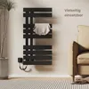 A black electric towel warmer is mounted on a light-colored wall in a room with a sofa and a potted plant. A striped towel is draped over one of the bars. Produktbild-Vorschau