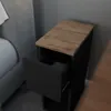 A narrow black nightstand with a wooden top and an open drawer, placed next to a bed. Podgląd zdjęcia produktu