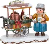 Ein fröhliches Winterkind in warmer Kleidung steht neben einem festlich geschmückten Punschwagen mit dampfendem Kessel und Tassen in der Hand bereit um heißen Punsch auszuschenken während Schnee auf dem Dach des Wagens liegt Produktbild-Vorschau