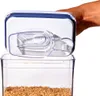 A hand is holding the lid of a clear food storage container with a blue rim, which is open and has a scoop inside. The container is filled with brown rice. Náhľad obrázku produktu
