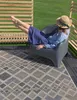 A person relaxing in a chair on a patio with a rug and wooden fence. Produktbild-Vorschau