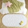 Weißer ovaler zotteliger Teppich auf hellem Holzboden, mit Bett und grüner Decke im Hintergrund Náhled obrázku produktu