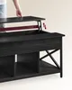 A person's hand is shown lifting the top of a black coffee table, demonstrating its lift-top feature. Produktbild-Vorschau