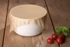 A white bowl covered with brown parchment paper sits on a wooden surface, with cherry tomatoes and basil leaves to the right. Náhled obrázku produktu