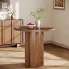 A round wooden dining table with a vase of greenery and a bowl of fruit on it, placed in a room with wooden furniture and flooring. Produktbild-Vorschau