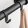 A close-up shot of a black metal coat rack with a beige sweater hanging on one of the hooks. Produktbild-Vorschau