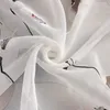 A close-up view of white sheer fabric with a black floral pattern. Produktbild-Vorschau