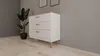 A white dresser with wooden accents and legs, placed next to a large potted plant in a modern room with light wood flooring and gray walls. Podgląd zdjęcia produktu