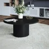 A black round coffee table with a fluted base, topped with a vase of white flowers, a magazine, and decorative geometric objects, placed on a fluffy white rug in a modern living room. Anteprima dell’immagine prodotto