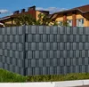 A fence made of anthracite PVC privacy screens for double-bar mesh fences, installed in a residential setting with houses and blue sky in the background. Náhled obrázku produktu