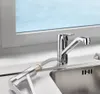 A chrome kitchen faucet with a pull-out spray hose attached, positioned over a stainless steel sink, with a window in the background. Produktbild-Vorschau