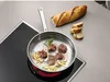 Lamb chops cooking in a pan on a stovetop, with a baguette and sliced bread nearby. Produktbild-Vorschau