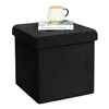 A black storage ottoman with a book and a mug on top, set against a white background. Produktbild-Vorschau