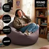 A young woman is sitting on a beanbag chair in a bedroom, listening to music with headphones. Voir les images du produit