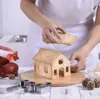 A person is assembling a gingerbread house with cookie pieces, surrounded by Christmas decorations and baking tools. Náhľad obrázku produktu
