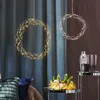 Two LED decorative wreaths hang in front of curtains, with a table displaying a plant arrangement and barware in the foreground. Produktbild-Vorschau
