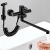 A black faucet with a sprayer is mounted on a wall above a white sink, with a hand washing under the running water. Podgląd zdjęcia produktu