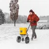 A person is pushing a yellow spreader in the snow. Produktbild-Vorschau