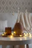 A decorative setup on a table with a vase, a candle holder, and string lights. Produktbild-Vorschau