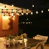 An outdoor patio table set up for an evening gathering, illuminated by string lights. Produktbild-Vorschau