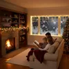 A family is reading a book by the fireplace and Christmas tree, with snow falling outside the window. Náhľad obrázku produktu