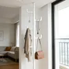 A white telescoping coat rack with several hooks, holding a jacket, two necklaces, and a brown handbag. The coat rack is positioned near a large window with a view of a balcony railing. In the background, a living room area with a sofa and coffee table is  Produktbild-Vorschau